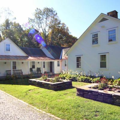 Sunlit white house with a garden and stone wall in a tranquil outdoor setting.