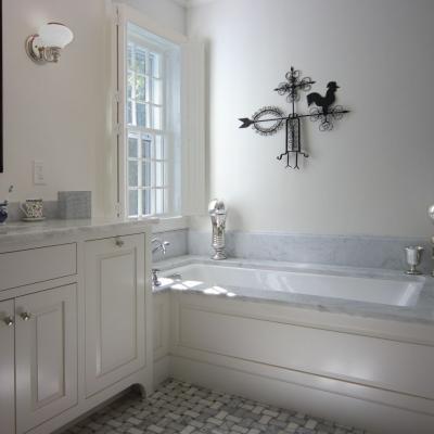 Stylish bathroom with a marble tub, white cabinetry, and decorative wall accents.