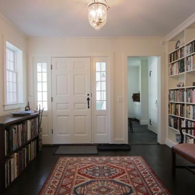 A bright entryway with a bookshelf, artwork, and a patterned rug.