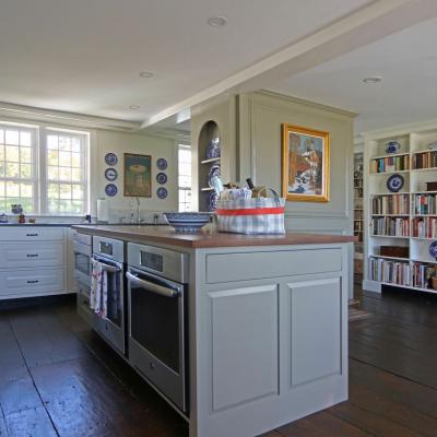 Bright kitchen with white cabinets, wood island, bookshelves, and decorative plates.