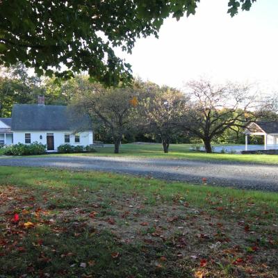 A white house with a gray roof, surrounded by trees and autumn leaves.