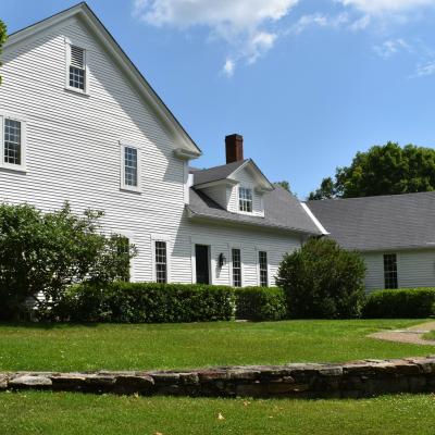White house with a gray roof, surrounded by green grass and shrubs, under a blue sky.
