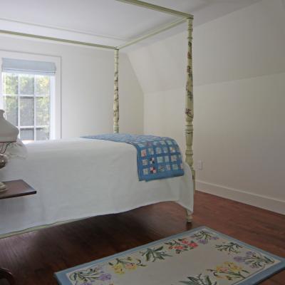 Bright bedroom with a four-poster bed, decorative quilt, lamp, and floral rug.