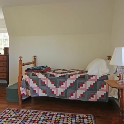 A cozy bedroom featuring a bed with a quilt, a dresser, and a bedside lamp.