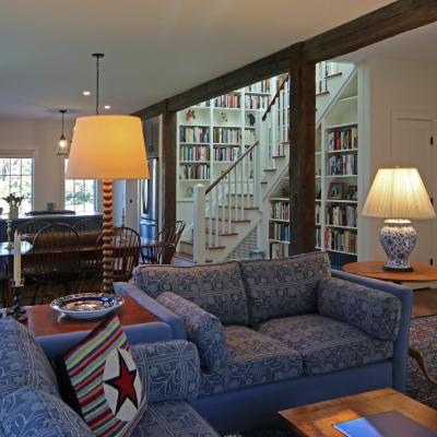 Cozy living room with blue couch, wooden table, and a view of a bookshelf and kitchen.