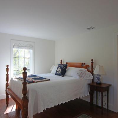 Bright bedroom with a wooden bed, quilt, and window, featuring a chair and bedside lamp.