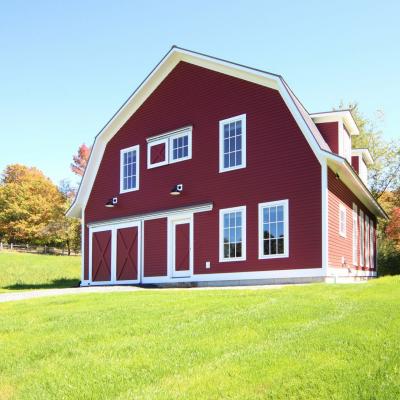 Red barn with white trim in a grassy field, surrounded by autumn trees.