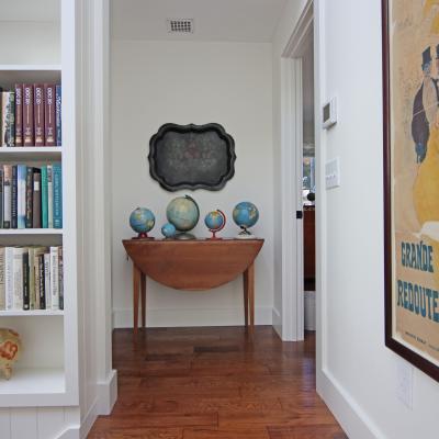 Narrow hallway with bookshelves, globes on a table, and a framed vintage poster.
