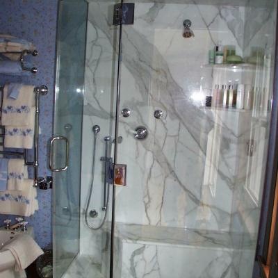 Modern glass shower stall with marble walls and various shower fixtures.
