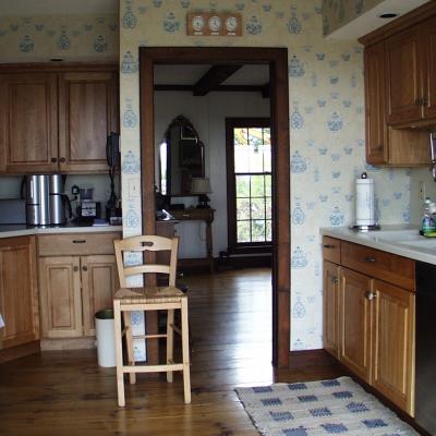 Cozy kitchen with wooden cabinets, an open doorway to a living area, and decorative wallpaper.