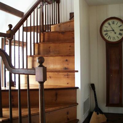 Wooden staircase with railings, a clock, and a musical instrument in the corner.