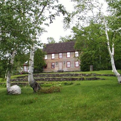 Two birch trees frame a rustic two-story house surrounded by green grass and stone landscaping.