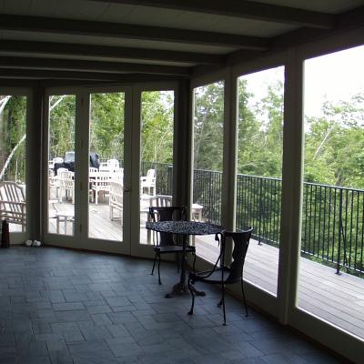 Screened-in porch with a table and chairs, overlooking a green, tree-filled landscape.
