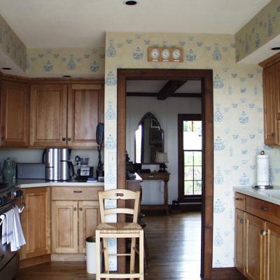 Cozy kitchen with wooden cabinets, decorative wallpaper, and a view into a dining area.
