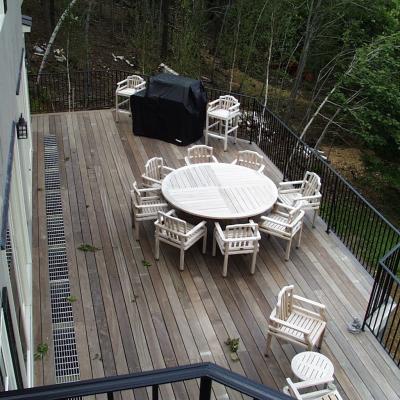 Outdoor deck with a circular table, chairs, and a black grill, surrounded by trees.