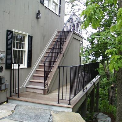 Exterior stairs leading to a deck, surrounded by trees and a beige house.