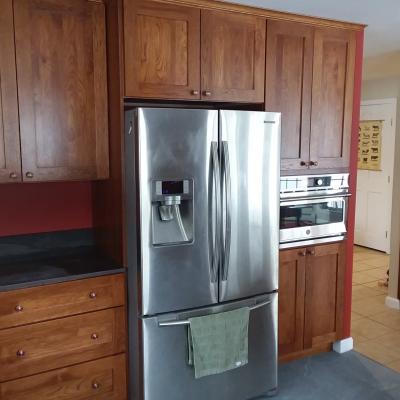 Modern kitchen with stainless steel refrigerator and wooden cabinetry against a red wall.