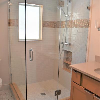 Modern glass shower enclosure with tiled walls and a hexagon floor. Natural light from window.