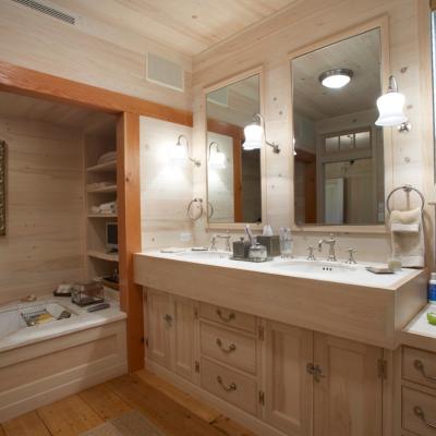 Wooden-themed bathroom with a double sink, mirrors, tub, and decorative artwork.