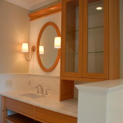 A bathroom vanity with a circular mirror, wooden cabinetry, and marble countertop.