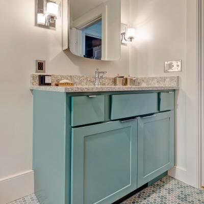 A modern bathroom vanity with teal cabinet, granite top, and round mirror.
