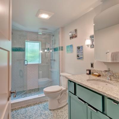Modern bathroom featuring a glass shower, teal cabinets, and hexagonal tile flooring.