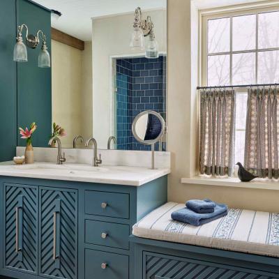 Modern bathroom with teal cabinetry, marble countertop, and patterned curtains.