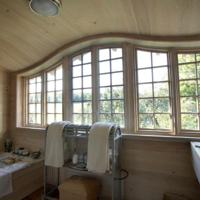 Cozy wooden bathroom featuring large windows, a tub, and neatly arranged towels.