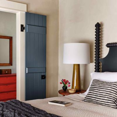 Cozy bedroom with a patterned bedspread, lamp, flowers, and a blue door.