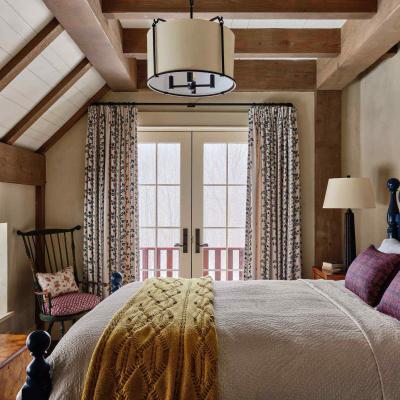 Cozy bedroom with a bed, patterned curtains, and wood accents. Natural light from double doors.