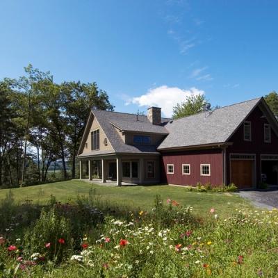 Red house with a gray roof surrounded by trees and colorful flowers under a blue sky.