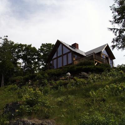 House on a hillside, surrounded by greenery and trees, under a cloudy sky.