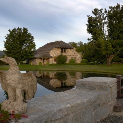 Stone house reflected in a pond, with a carved eagle statue in the foreground.