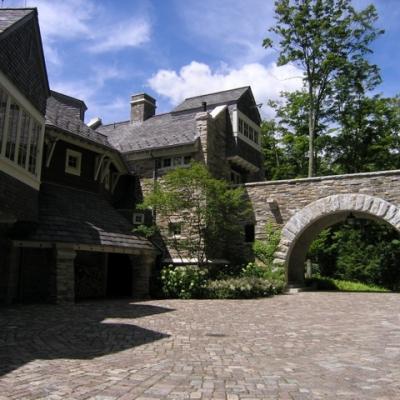 Stone mansion with a curved arch bridge and lush greenery under a blue sky.