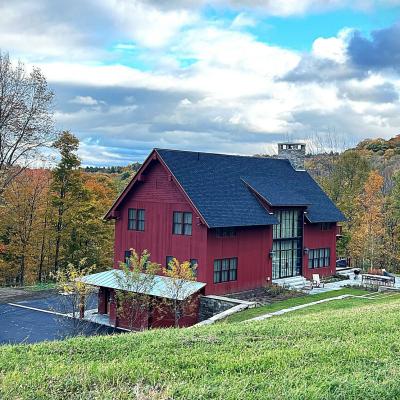 Modern red house on a hillside surrounded by colorful autumn trees.
