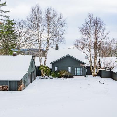 Snow-covered home and outbuilding surrounded by trees in a winter landscape.