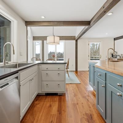 Modern kitchen with blue and white cabinetry, stainless appliances, and wooden floors.