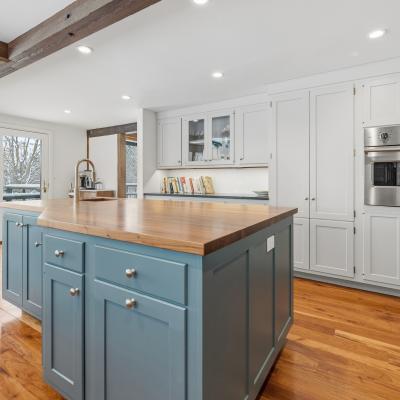 Modern kitchen with a blue island, wooden countertop, and white cabinets. Natural light flows in.