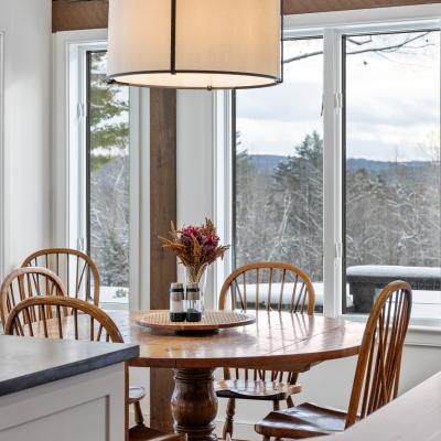 Cozy dining area with a round table, four wooden chairs, and large snowy windows.