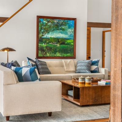 Stylish living room with a light sofa, colorful pillows, a coffee table, and a landscape painting.
