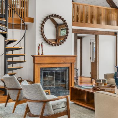 Modern living room with spiral stairs, fireplace, and stylish furniture. Natural light flows in.