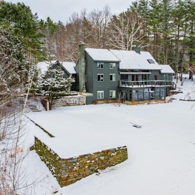 A large gray house surrounded by snow-covered ground and trees.