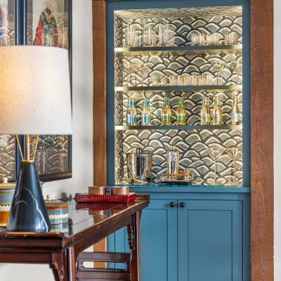 A stylish blue cabinet displays glasses and bottles, placed beside a wooden table and lamp.