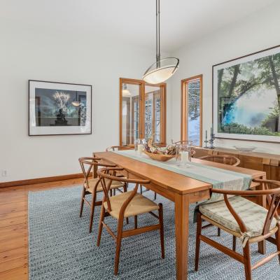 Bright dining room with wooden table, chairs, and artwork on the walls. Natural light from windows.