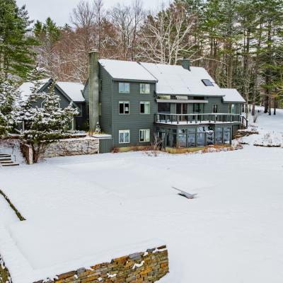Snow-covered landscape with a large, dark house and surrounding trees.