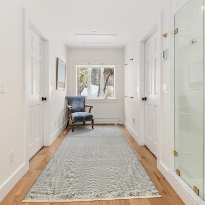Bright hallway with a blue chair, wood flooring, and a glass shower.