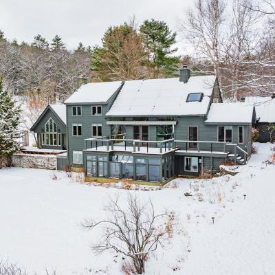 Modern house with a deck, surrounded by snow and trees, under a cloudy sky.