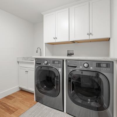 Modern laundry room featuring gray washer and dryer, white cabinets, and marble countertop.