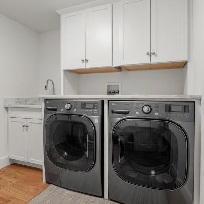 Modern laundry room with gray washer and dryer, white cabinets, and a light wood floor.