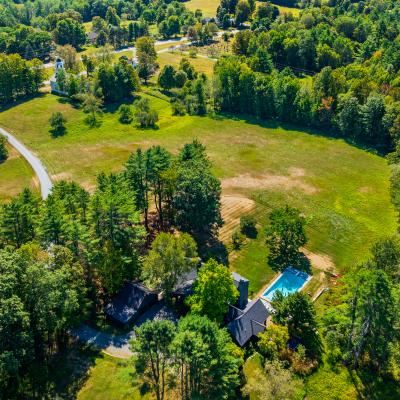 Aerial view of a house surrounded by greenery and a pool in a spacious landscape.